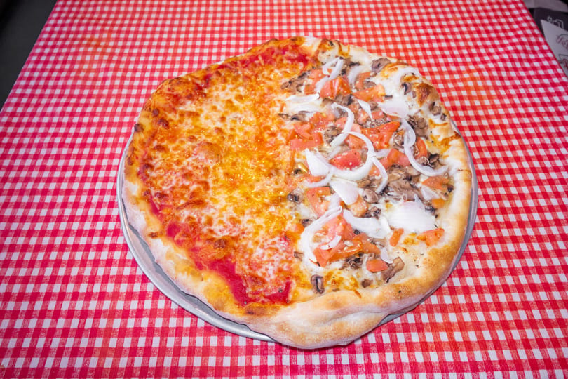 Half cheese, half mushroom, tomato, and onion pizza on a red and white checkered tablecloth.