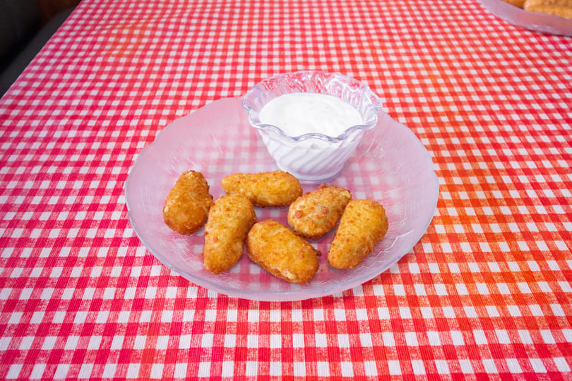 Seven golden-brown fried appetizers and a small bowl of white dipping sauce on a clear plate.